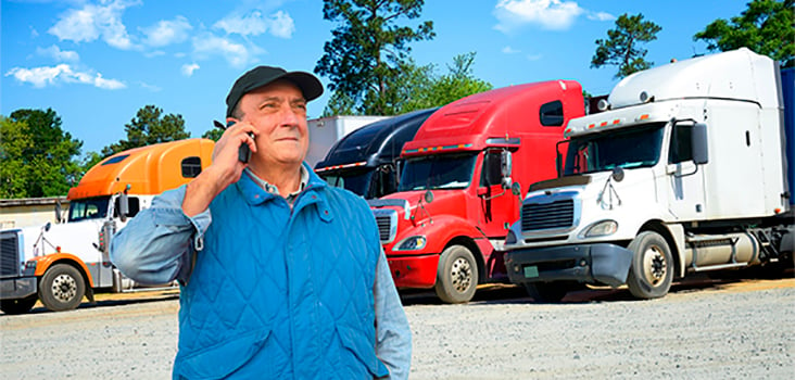Male truck driver standing in front of semi-trucks and talking on phone