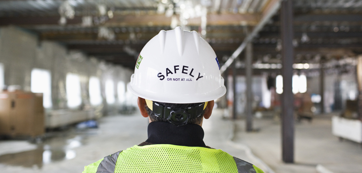 Worker wearing a white hard hat that reads "SAFELY or not at all"