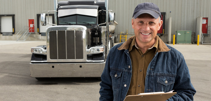 CDL certified truck driver holding a clip board in front of his truck.