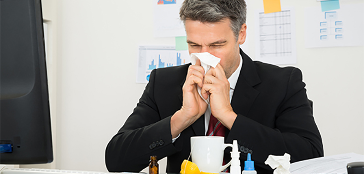 Man dressed in professional attire blowing nose into tissue