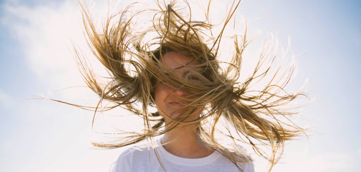 Woman standing in front of the sun with her hair being blown by the wind