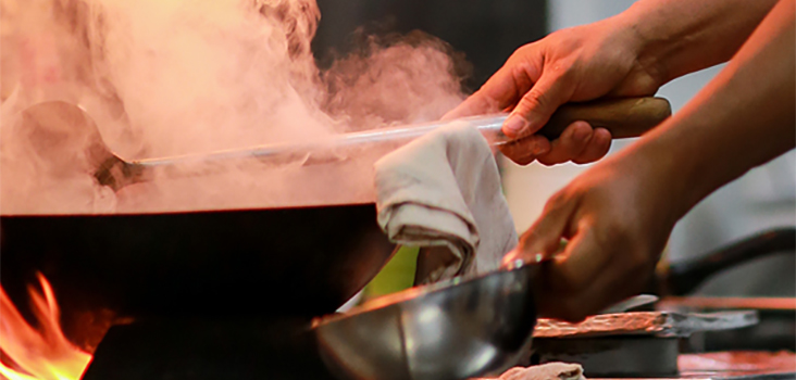 Chef works with a steaming wok under a fire