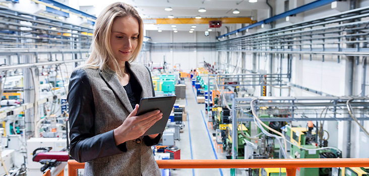 Woman holding ipad in manufacturing plant, reading manufacturing news.