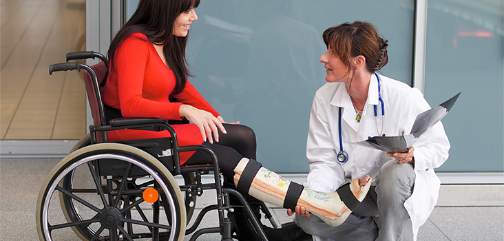 Female physician assisting woman in wheelchair with leg cast