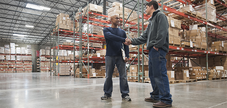 Two male workers shaking hands in a warehouse