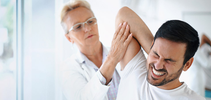 Female physician stretching male's arm as his face is in pain.